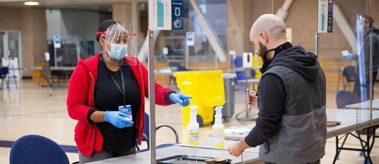 One person giving another person supplies to conduct a covid test on themselves.