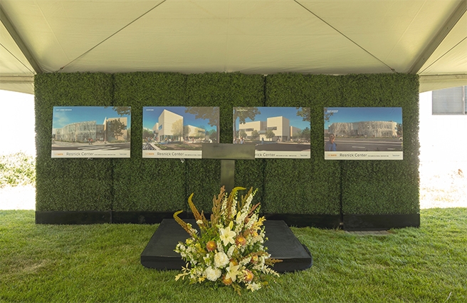 Renderings of the Lynda and Stewart Resnick Center for Agricultural Innovation on a grassy backdrop in front of a short podium with a large flower arrangement in front.