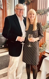 Eivind Lange and Mary Puma pose in semi-formal attire inside a restaurant each holding a glass of wine.