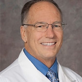 Dr. Charles DeCarli wearing a white coat and glasses in front of a dark grey wall.