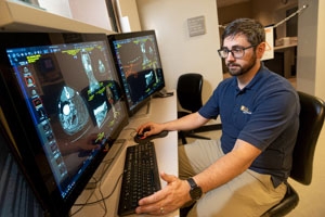 Michael Brown, a fourth-year resident in radiology at the UC Davis School of Veterinary Medicine wearing a navy polo and khakis, examining imaging scans of a dog.