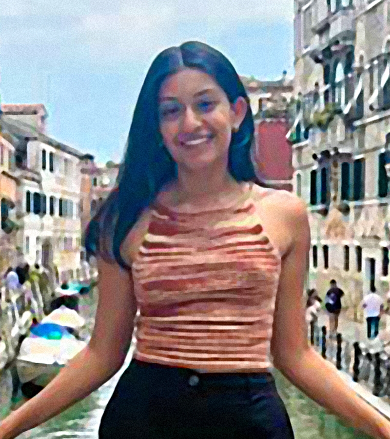 Amrit Bains poses in a velvet sleeveless top and dark pants in front of a Venetian canal.